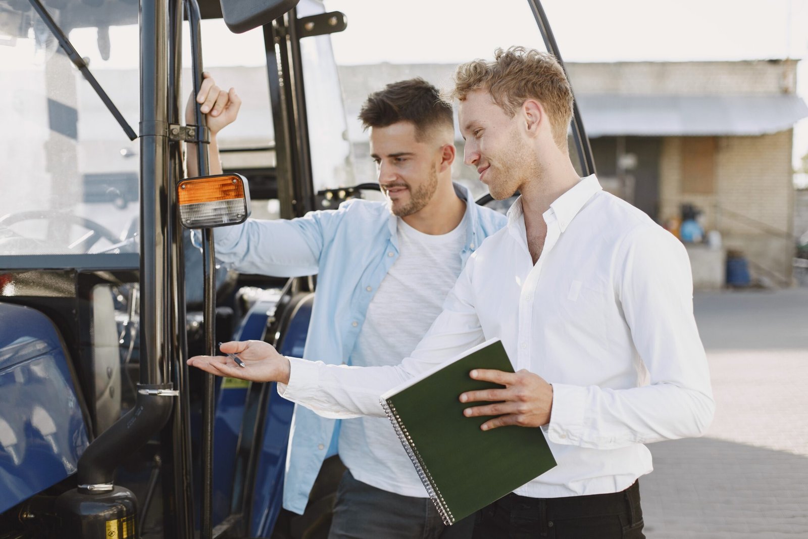 Two men conducting a pre-purchase inspection of agricultural machinery, examining a tractor and taking notes before buying.